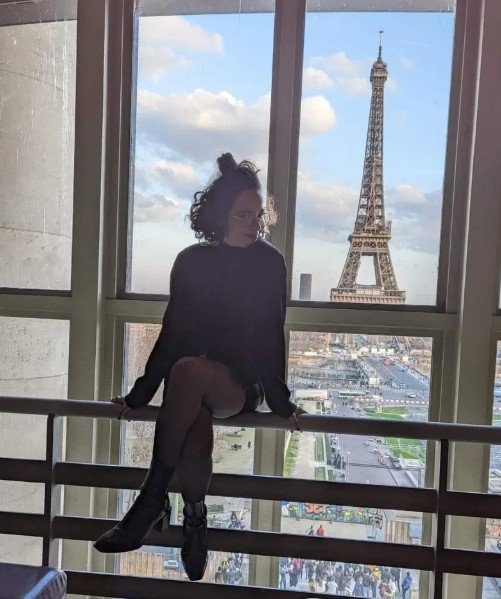 Kenza Talbi, alias Raven, assise devant une fenêtre face à la tour Eiffel